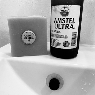 Une bouteille de bière sur le lavabo avec un savon de bière. Dans le lavabo un porte-savon aimanté. La capsule de la bouteille de bière est dans le savon